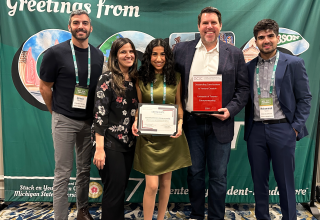 Members of U of T Entrepreneurship community holding an award and a certificate in front of a green GCEC backdrop.